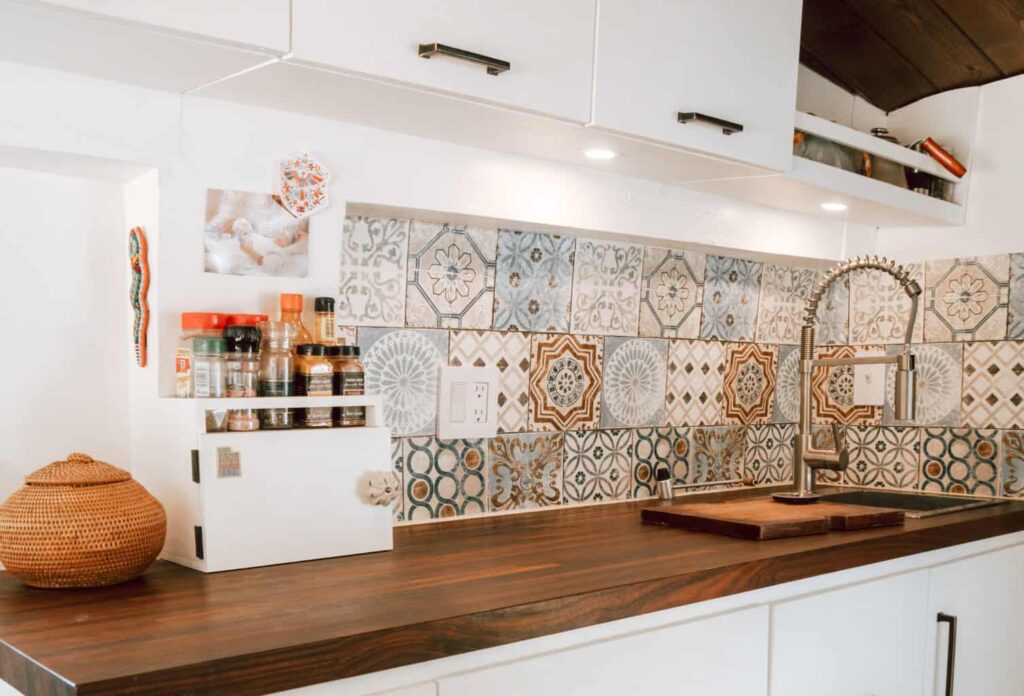Camper van kitchen with vinyl faux-tile backsplash, sink, faucet, and spice rack