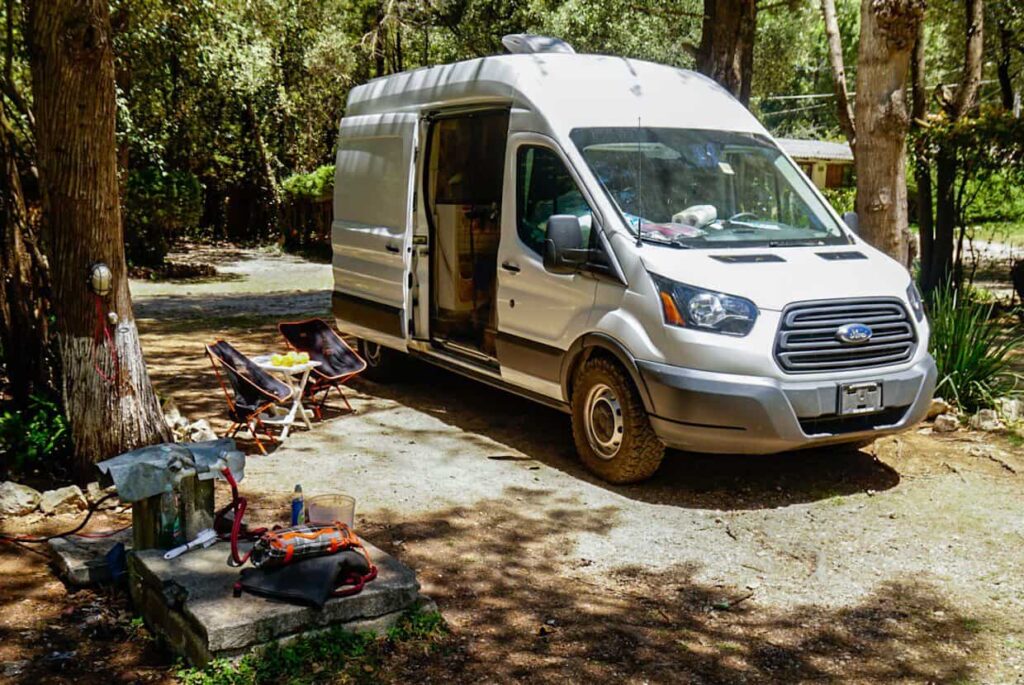 Ford Transit camper van parked under trees in a paid campground