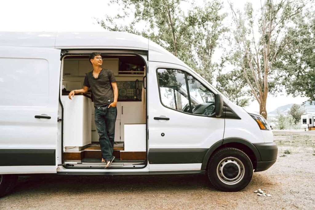 Man standing inside a Ford Transit camper van looking out the side door