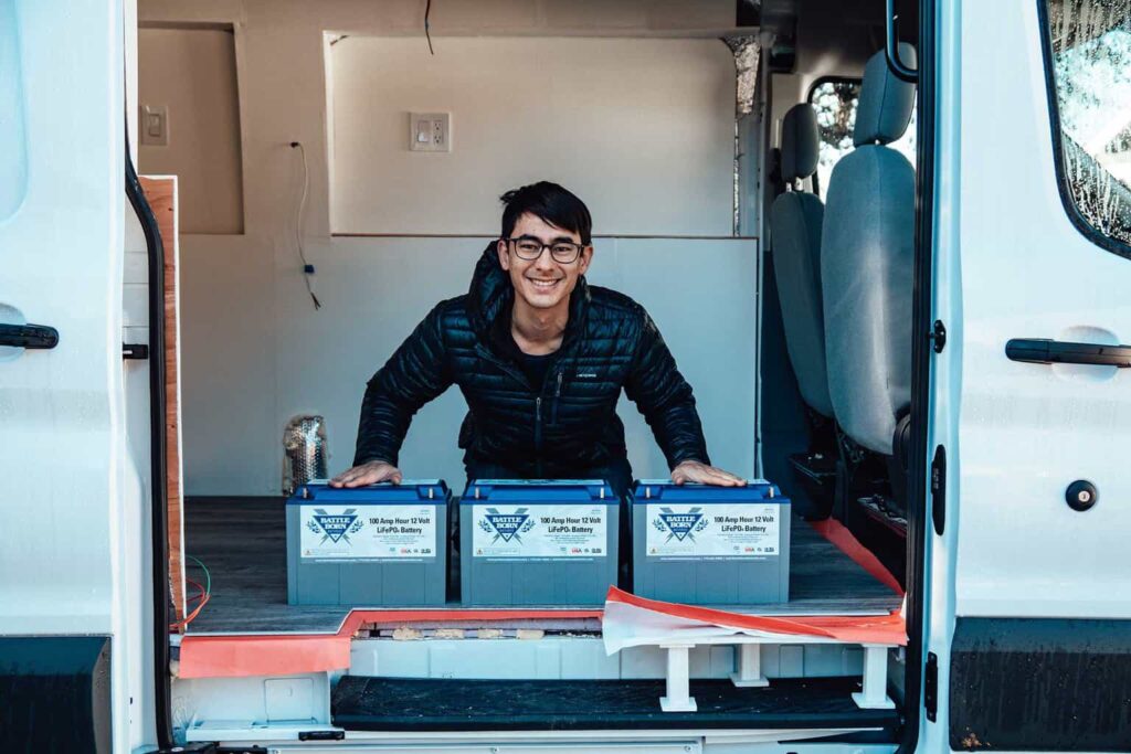 Man sitting behind three Battle Born camper van leisure batteries inside a Ford Transit camper van