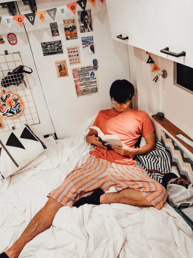 Boy reading next to a reading light on the bed, inside a Ford Transit camper van