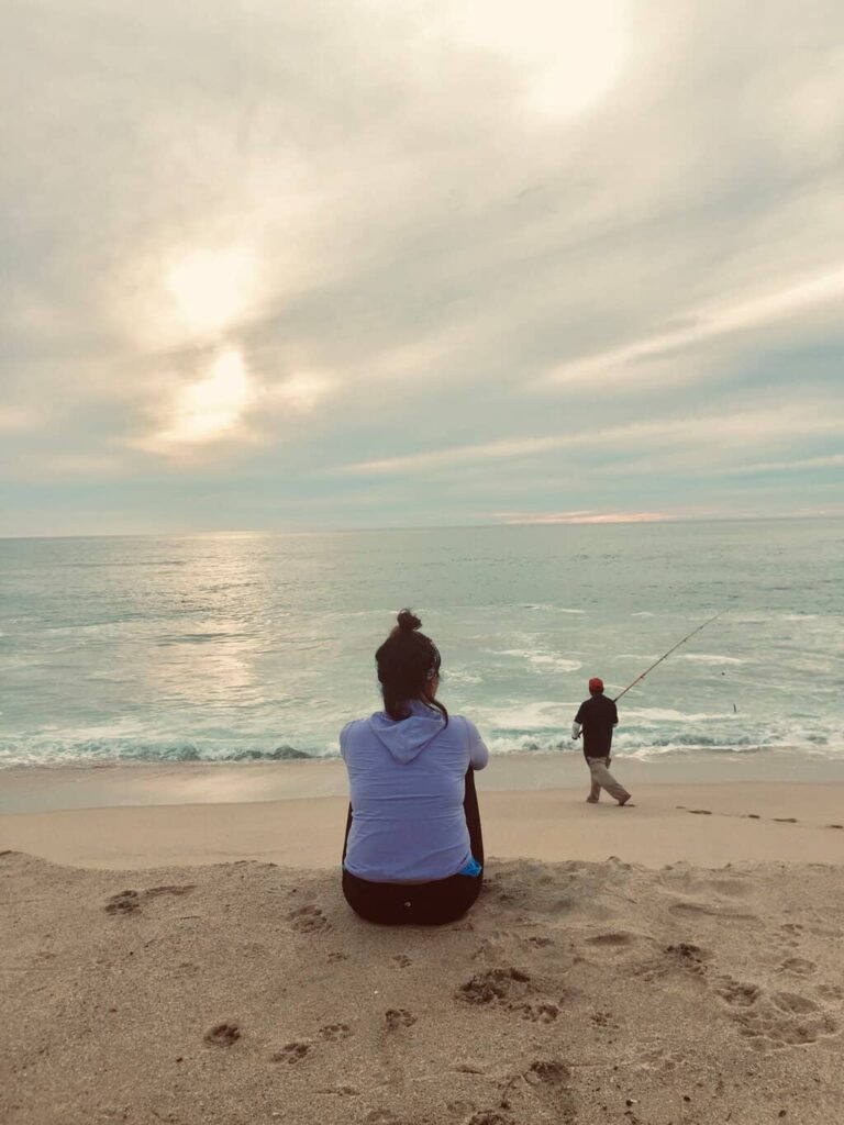 Yuko sitting on the sand watching the ocean and a fisherman