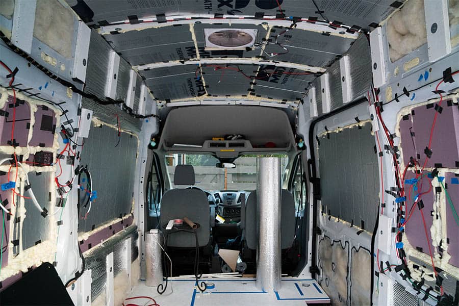 Camper van interior showing unfinished conversion with insulation, elecrical wire, and furring strips