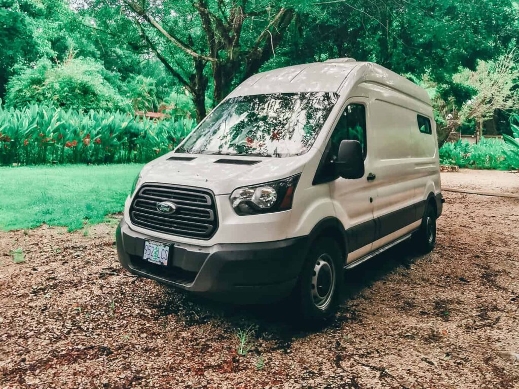 White Ford Transit camper van parked on dirt lawn