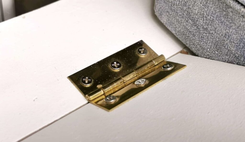 Brass hinge screwed onto white plywood board