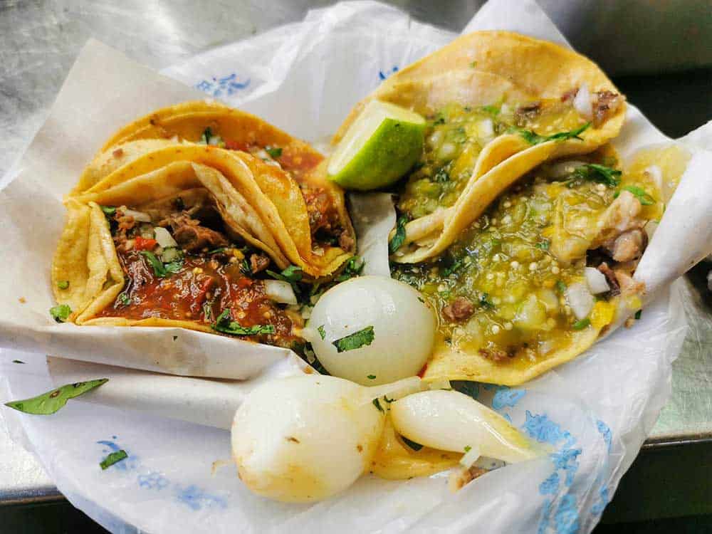Two small mexican tacos slathered in salsa and guacamole sauce