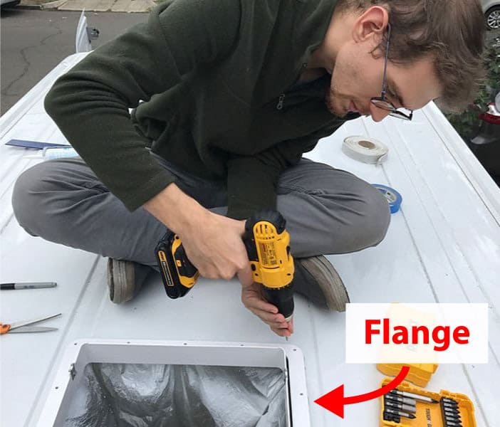 Man screwing the vent fan flange to the camper van roof.