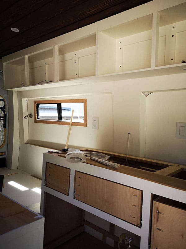 Half-built camper van with kitchen counter and overhead cabinets
