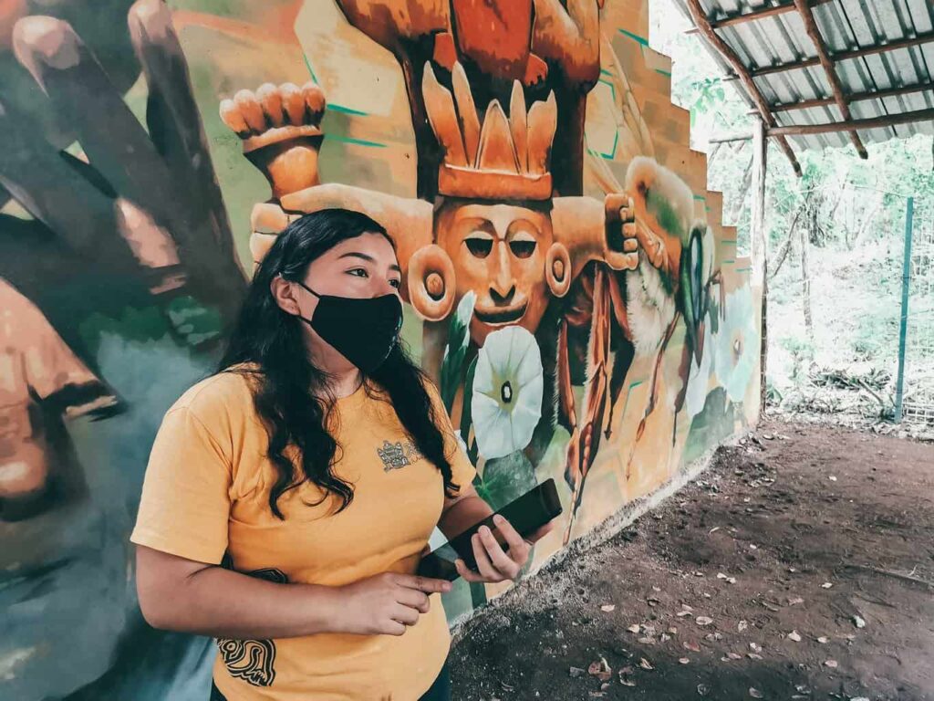 Tour guide standing behind a Mayan mural