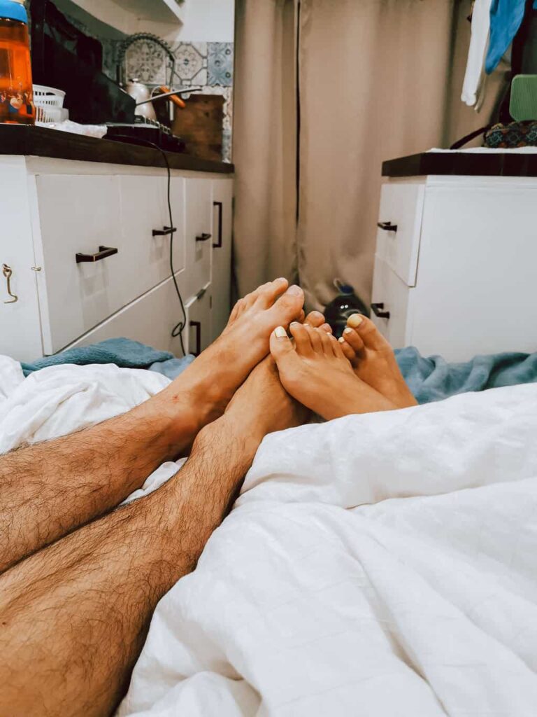 Two pairs of feet on the bed inside a camper van
