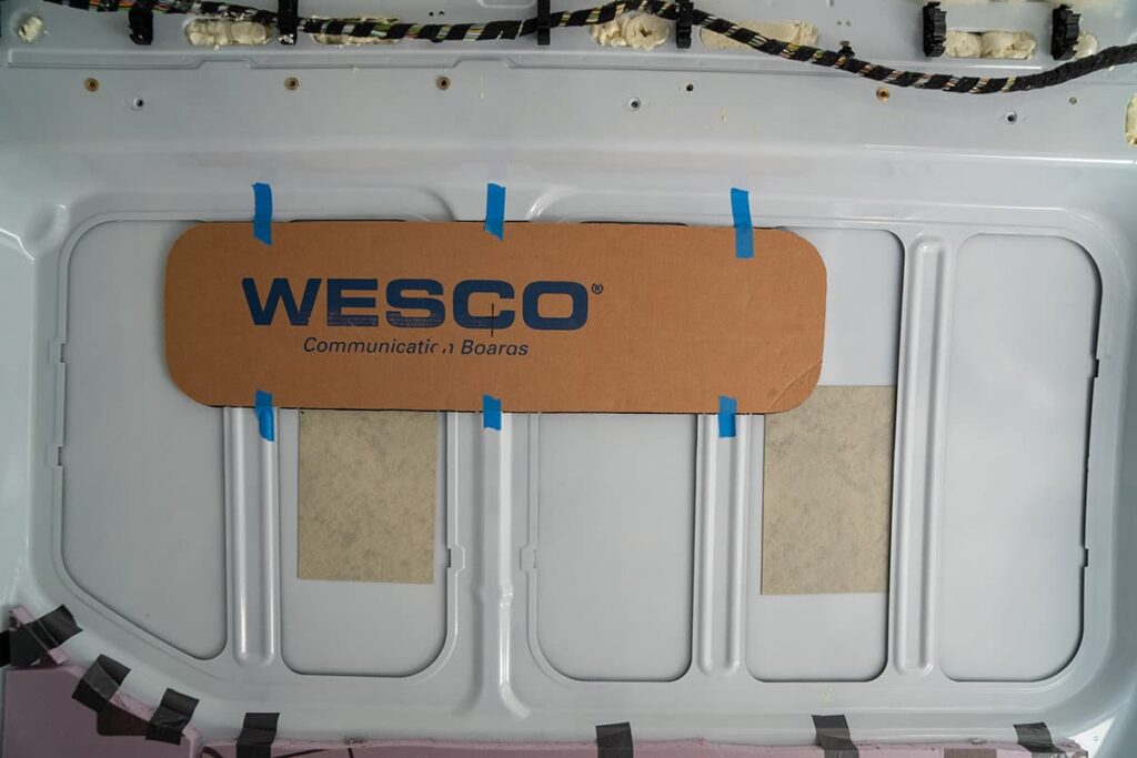 A cardboard template of an RV window being taped up inside a camper van
