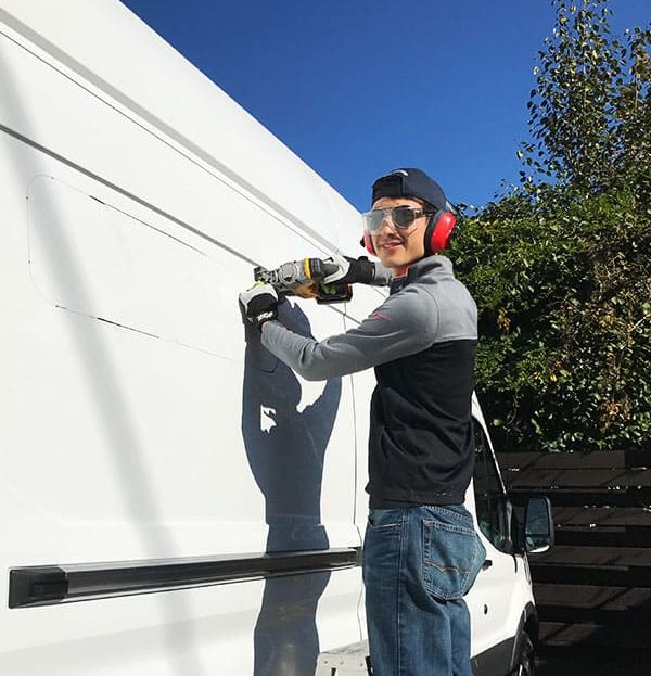 Eric using a jig saw to cut a hole in our van's wall to install the window