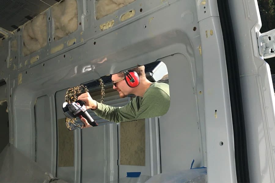 Man filing the metal edge of the window hole in a camper van