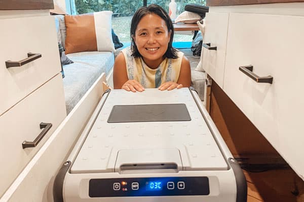 Woman kneeling behind a 12V fridge in a camper van